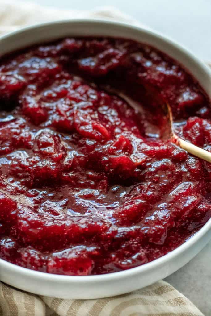 Close up of a bowl of baked cranberry sauce with a gold spoon tucked in.