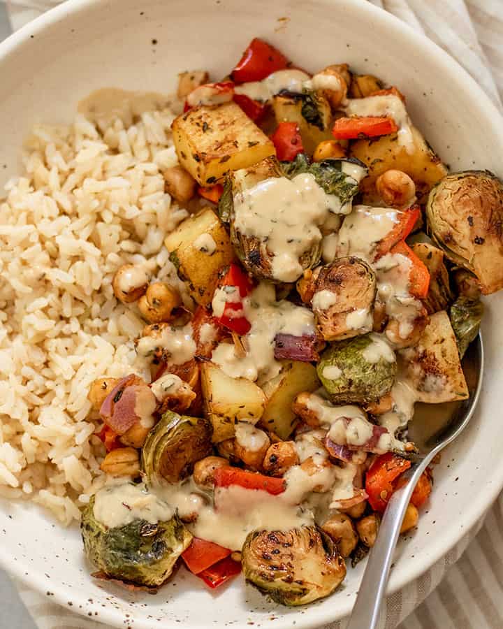 Roasted vegetables and chickpeas served in a white bowl with brown rice and dressing.