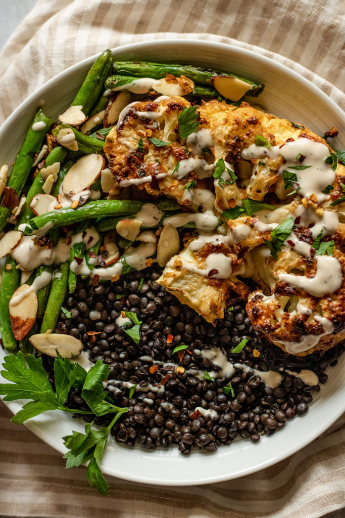 Plate of lentils, green beans and roasted cauliflower topped with tahini dressing.