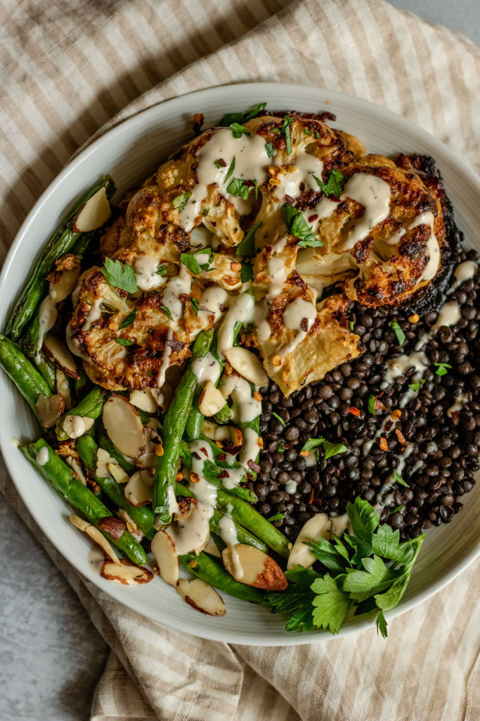 Roasted cauliflower topped with sauce and served with lentils and green beans.