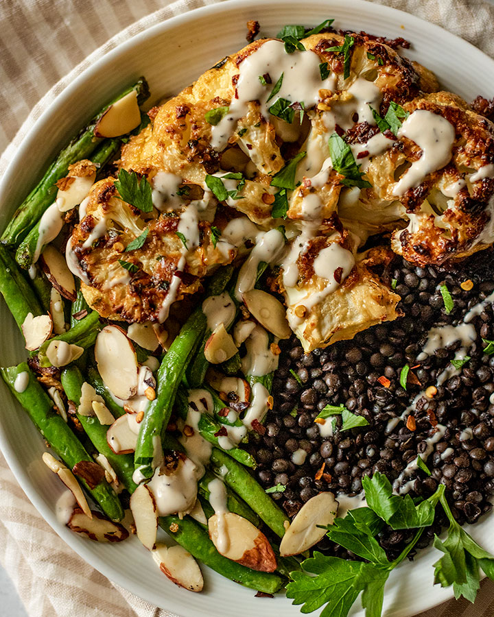 Close up view of tahini roasted cauliflower plated with lentils and green beans.