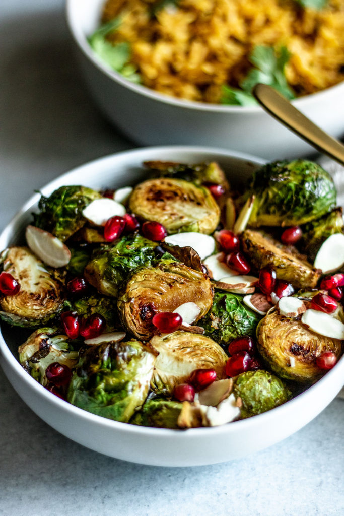Side view of a bowl of roasted brussels sprouts, pomegranate and almond slices.