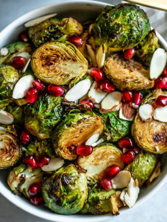 Close up bowl of roasted brussels sprouts topped with pomegranate seeds and almond slivers.