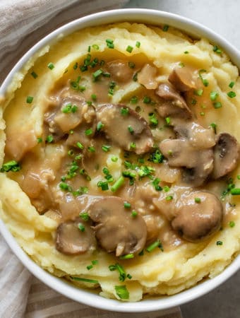 White bowl of mashed potatoes covered in miso mushroom gravy.