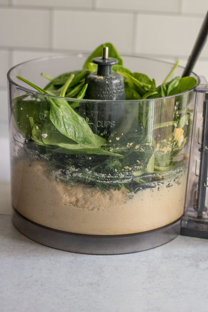 Stuffing herbs and spinach into a food processor to mix with tofu ricotta.