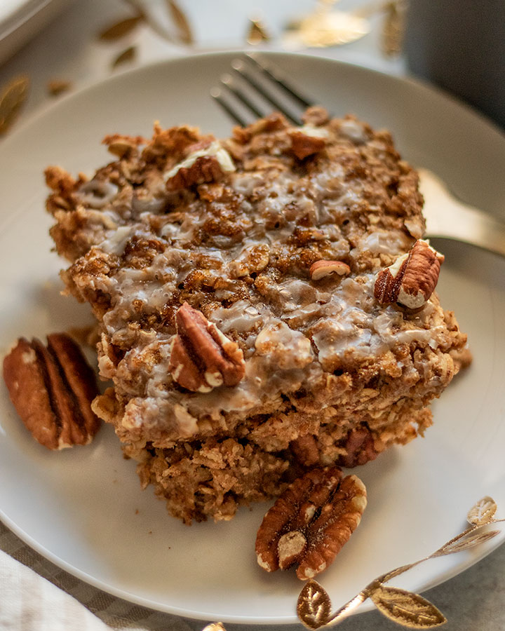 Close up of a slice of baked oatmeal topped with icing and pecans.