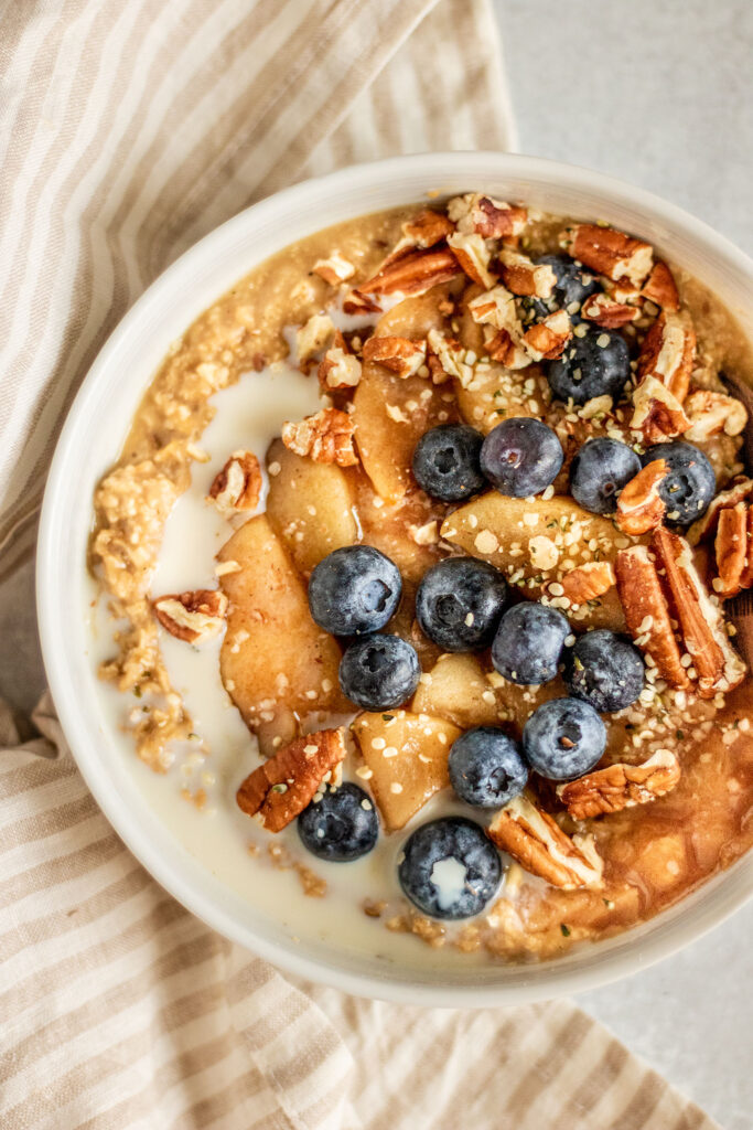 Bowl of oatmeal topped with slow cooker baked apples, berries and pecans with a splash of milk.