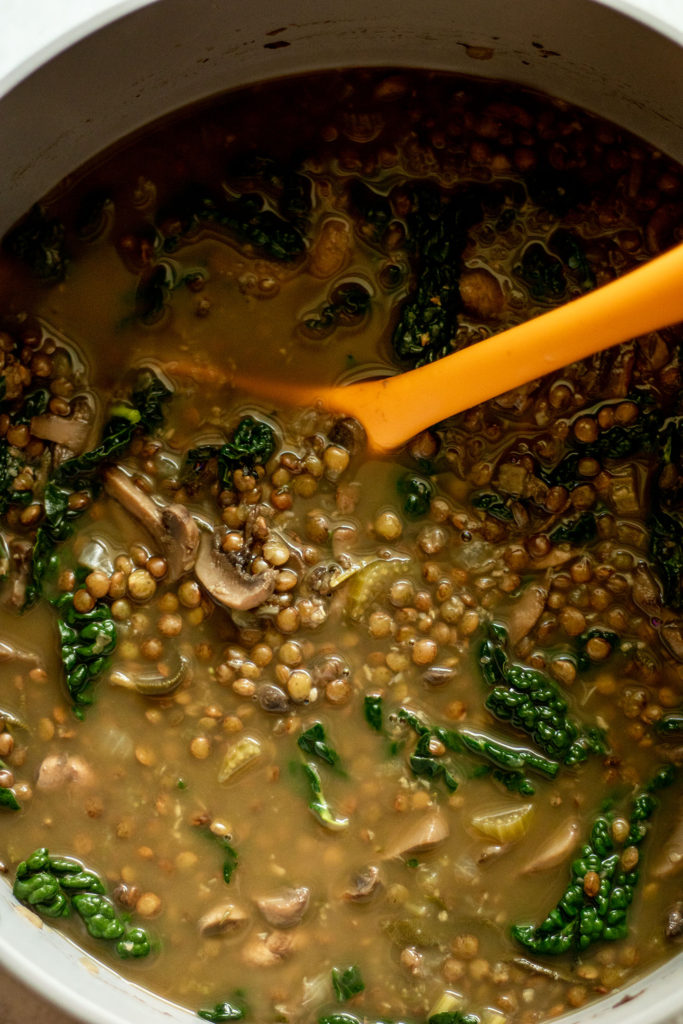 Lentil soup after cooking with wilted kale being stirred in.