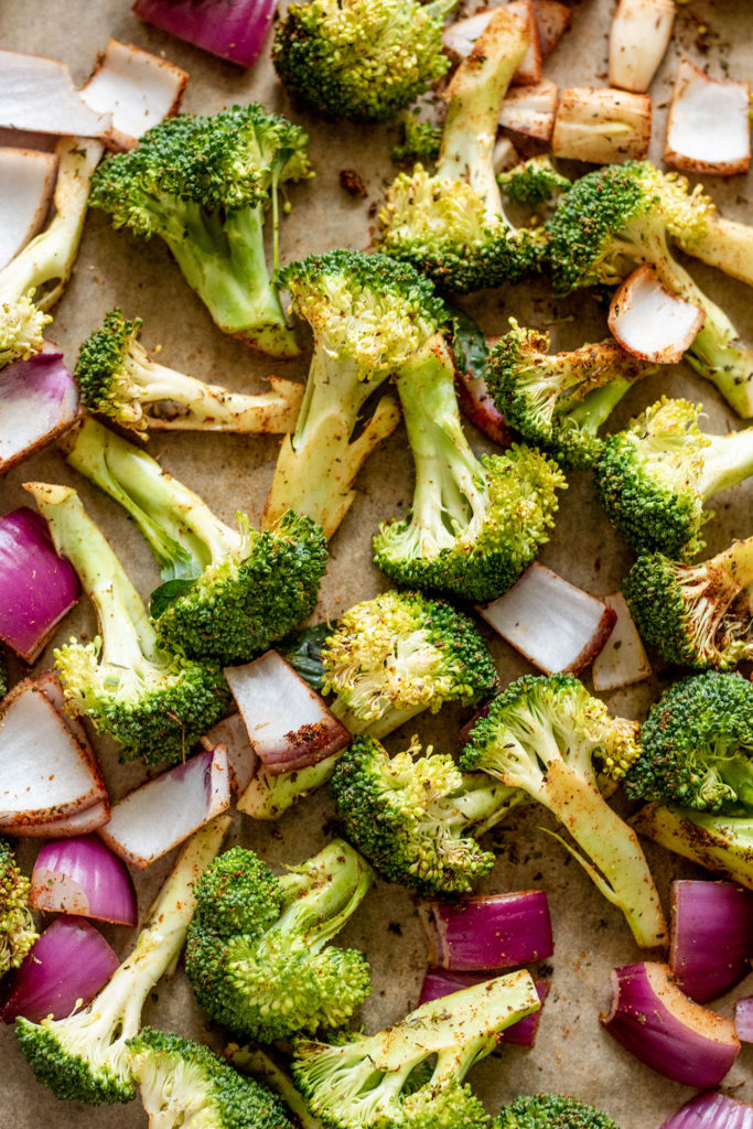 Broccoli and onion coated with spices and ready to roast.