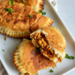 Fried pasteliots on a rectangular plate with the front pastry torn in half to show the filling.