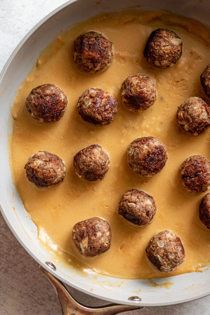 Meatballs placed on top of some gravy in a pan.