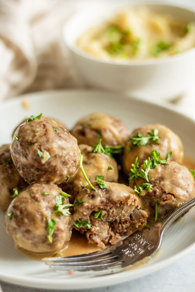 Meatballs topped with gravy with a fork cutting into one of the front meatballs.