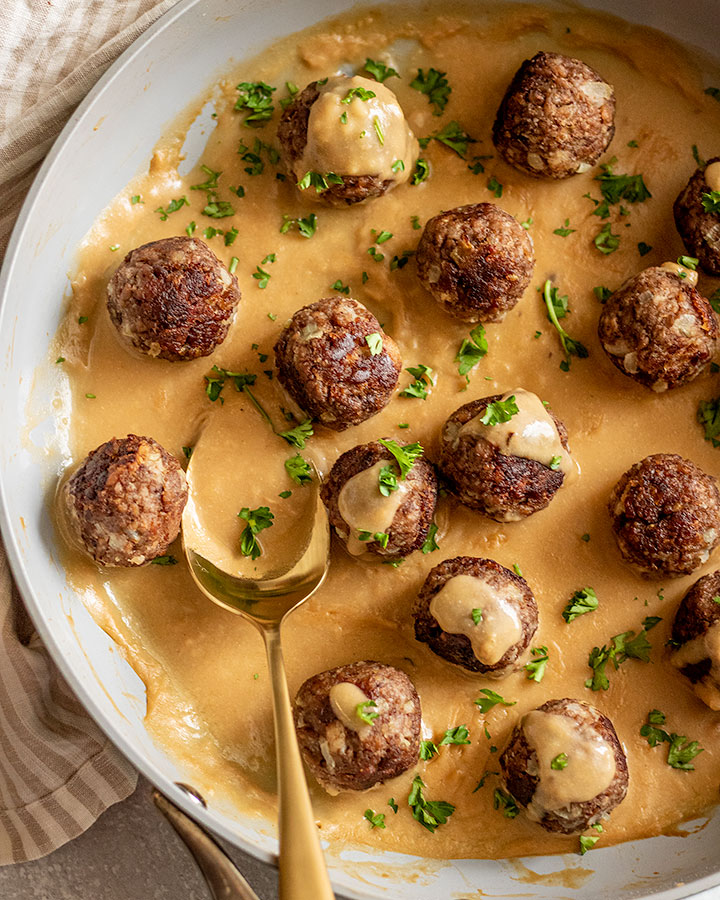 Pan of Swedish meatballs coated in gravy with a ladle of gravy on the side.