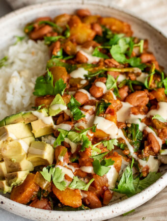 Close up of a bowl of pinto bean stew served with rice, avocado and cilantro.