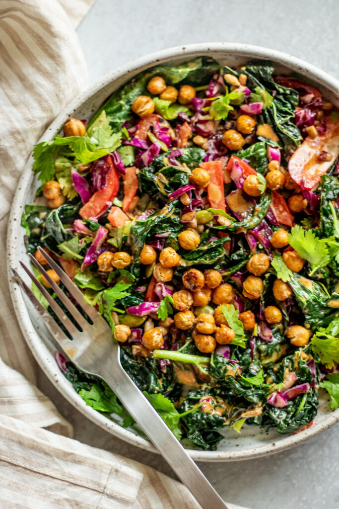 A fork sitting in a bowl of salad topped with chickpeas and peanut sauce.