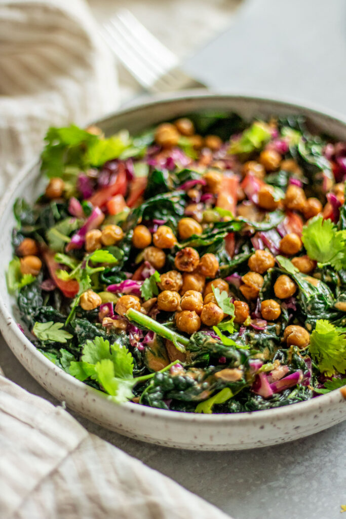 Side view of a crunchy salad loaded with kale, cabbage, bell pepper, chickpeas and peanut sauce.