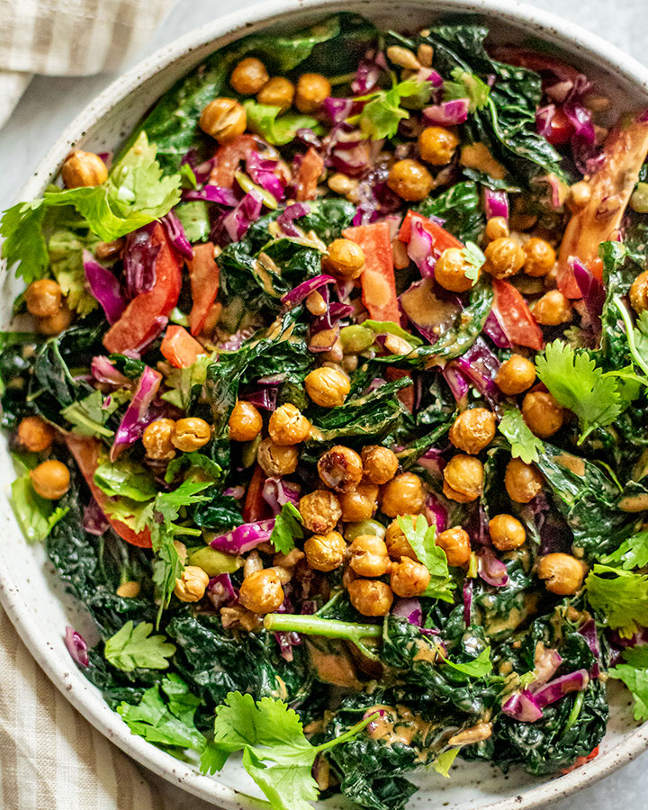 Close up of a kale crunch salad topped with chickpeas and peanut sauce.