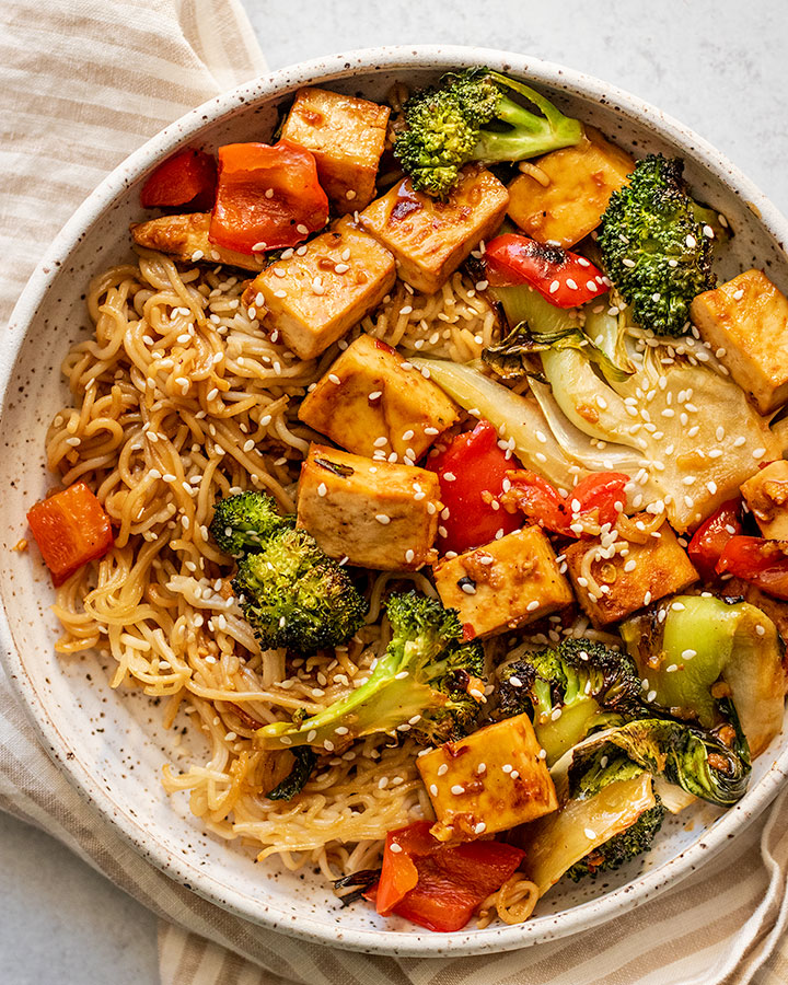 Sheet pan maple soy glazed tofu and noodles plated in a speckled bowl with a napkin in the background.