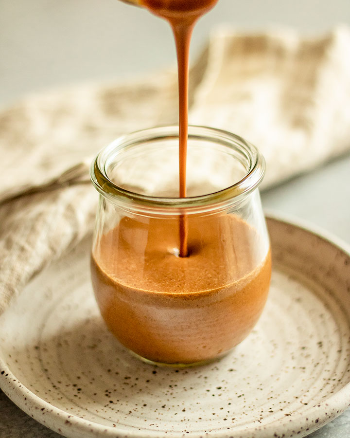 Pouring peanut sauce into a jar sitting on a plate.