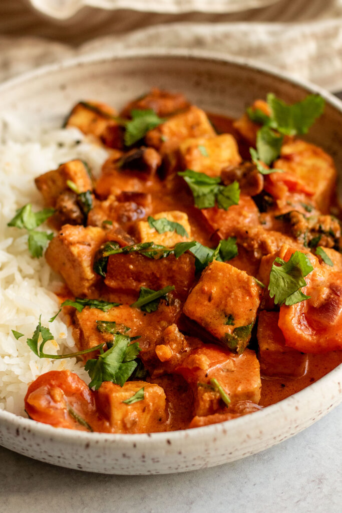 Side view of a bowl of peanut curry topped with cilantro and served with rice.