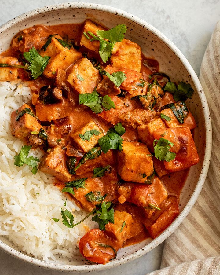 Top down view of a bowl of peanut red curry plated with white rice and topped with cilantro.