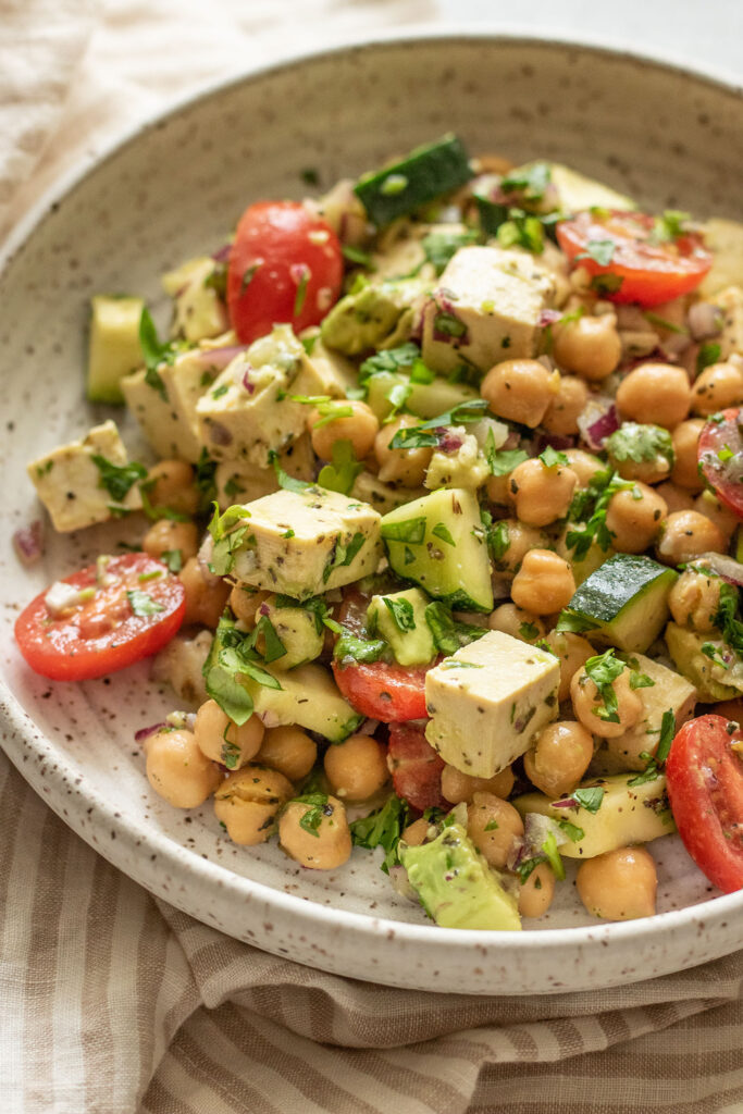 Side view of a plate of avocado chickpea salad topped with extra fresh herbs.