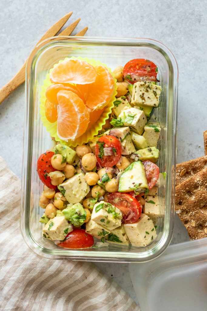 Lunch container with chickpea salad, a divider with orange slices and whole grain crackers to the side.