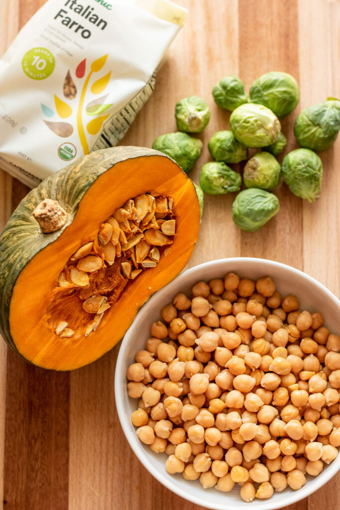 Cutting board with farro, kabocha squash, brussels sprouts and a bowl of rinsed chickpeas.
