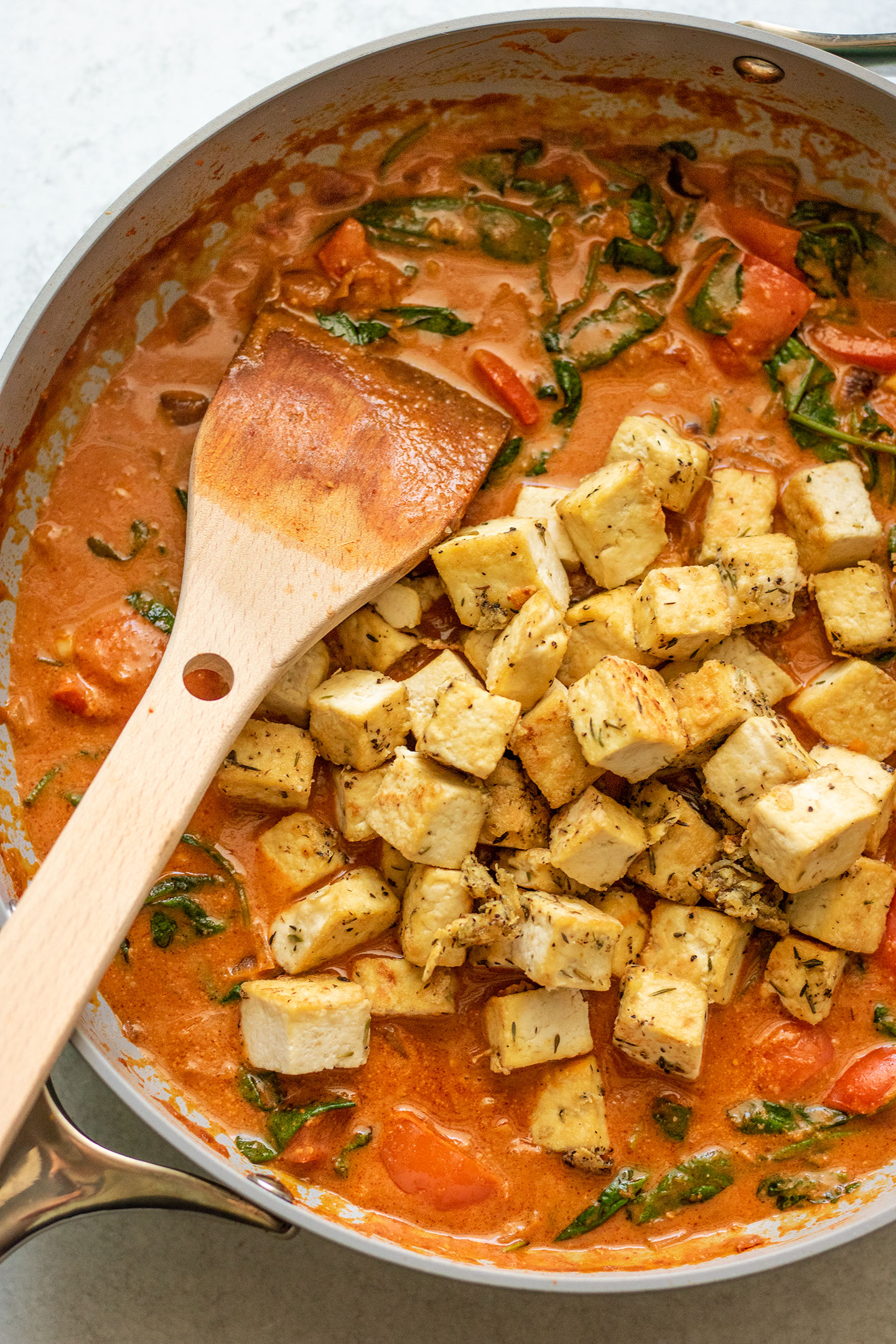 Adding the golden tofu to the pan with the red peanut curry sauce.