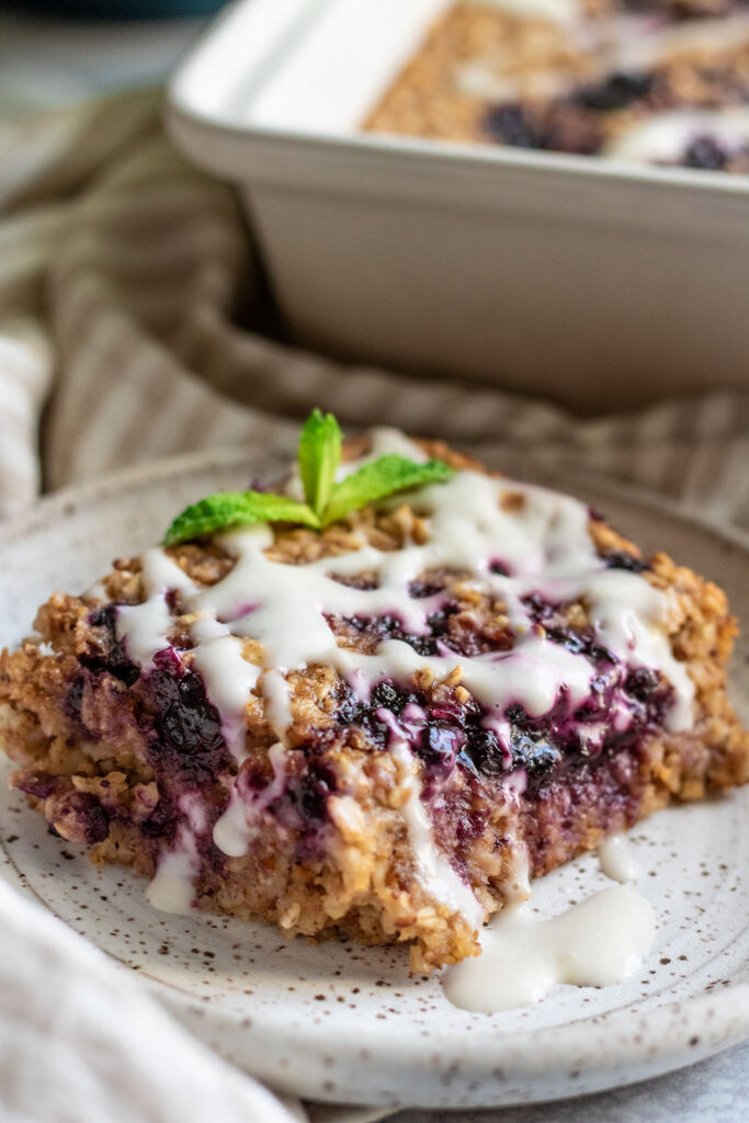 Close up view of a square of baked oatmeal topped with vegan lemon yogurt and a fresh mint leaf.