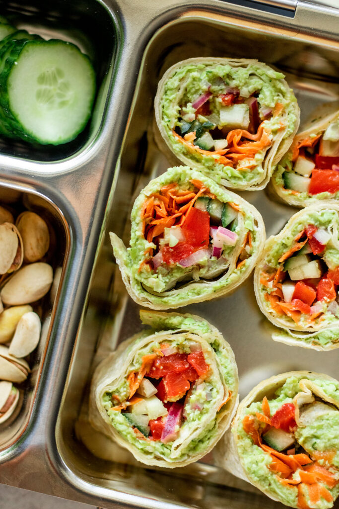Veggie wrap cut into pieces and placed in a lunch box with cucumber, golden berries and pistachios.