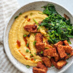 Bowl of polenta, spinach and tempeh on a stripped napkin.