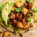 A single taco on parchment paper topped with lentils, roasted potatoes and avocado slices.