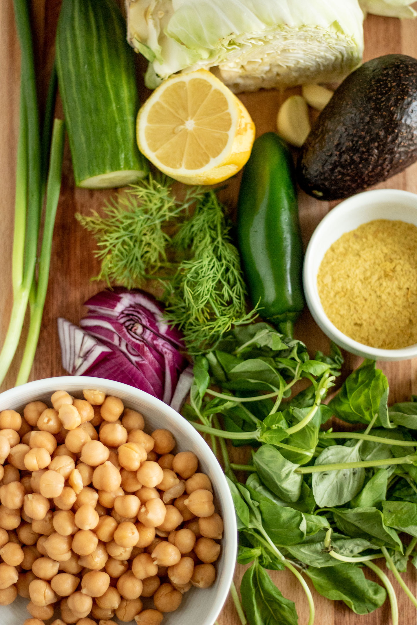 Salad dressing ingredients and sandwich ingredients on a cutting board including fresh herbs and chickpeas.