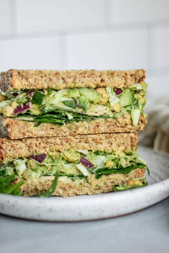 Side view of a chickpea salad on whole grain bread served with spinach, hummus and mustard.