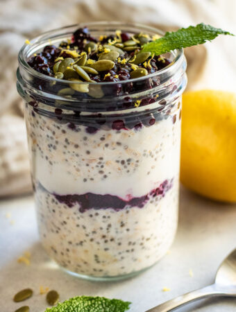 Close up of a jar of lemon blueberry overnight oats topped with pepitas and a fresh lead of mint.