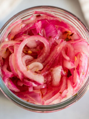 Jar of fully pickled onions, softened and vibrant pink in color.