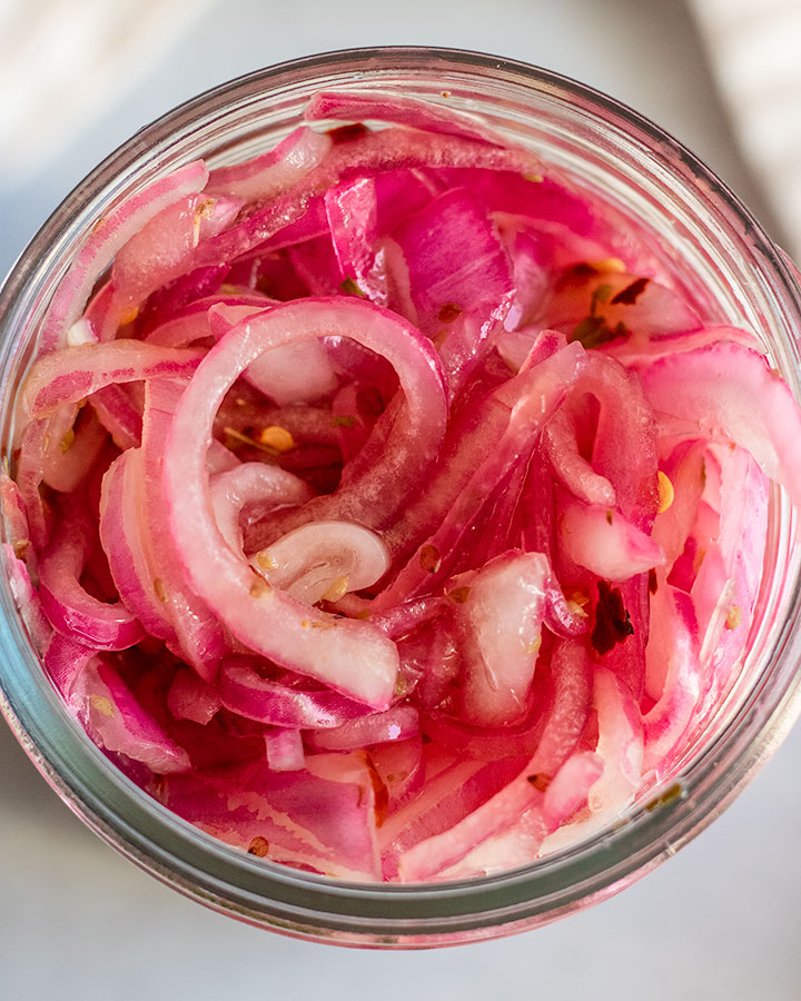 Jar of fully pickled onions, softened and vibrant pink in color.