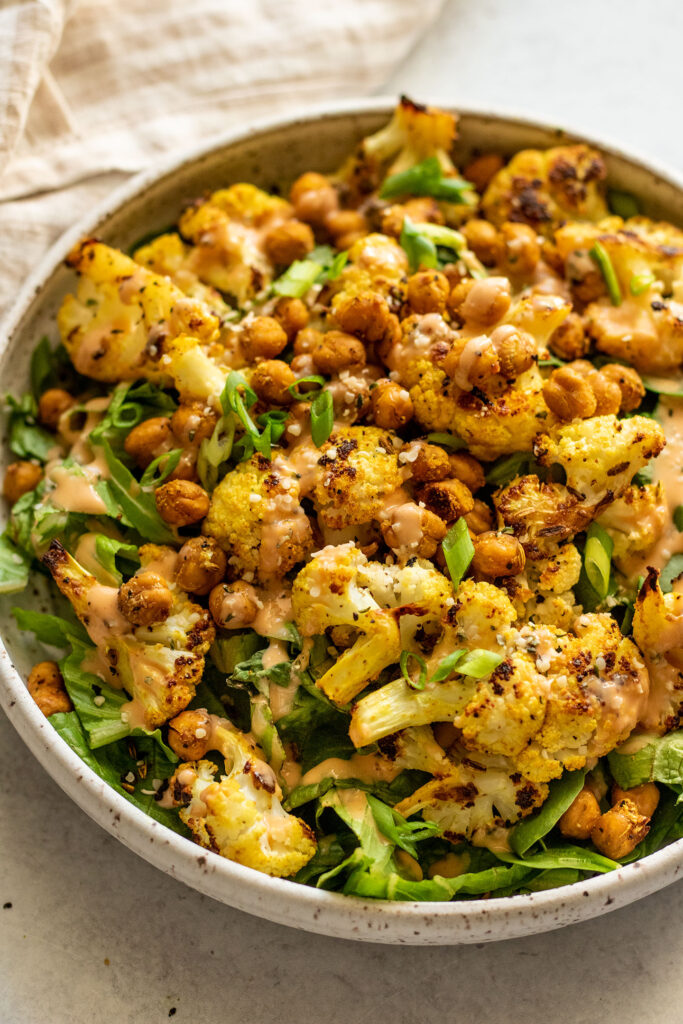 Side view of a bowl of greens, cauliflower and crispy chickpeas.