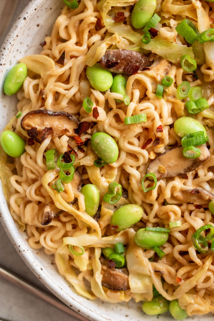 Close up of a bowl of peanut butter noodles tossed with spicy peanut sauce, edamame and mushrooms.