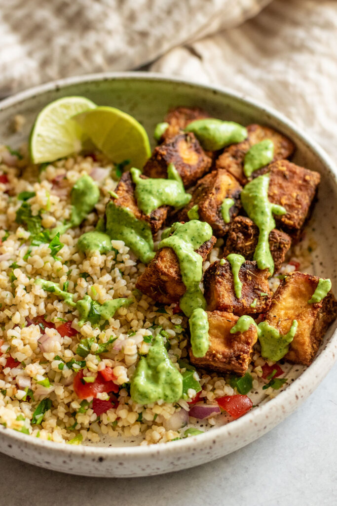 Side view of a bowl of Tipili salad served with tofu and cilantro sauce.