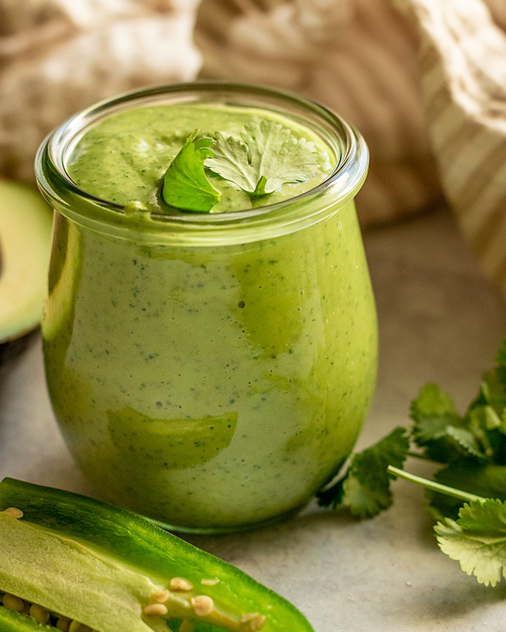 Jar filled with cilantro lime dressing topped with a few leaves of cilantro.