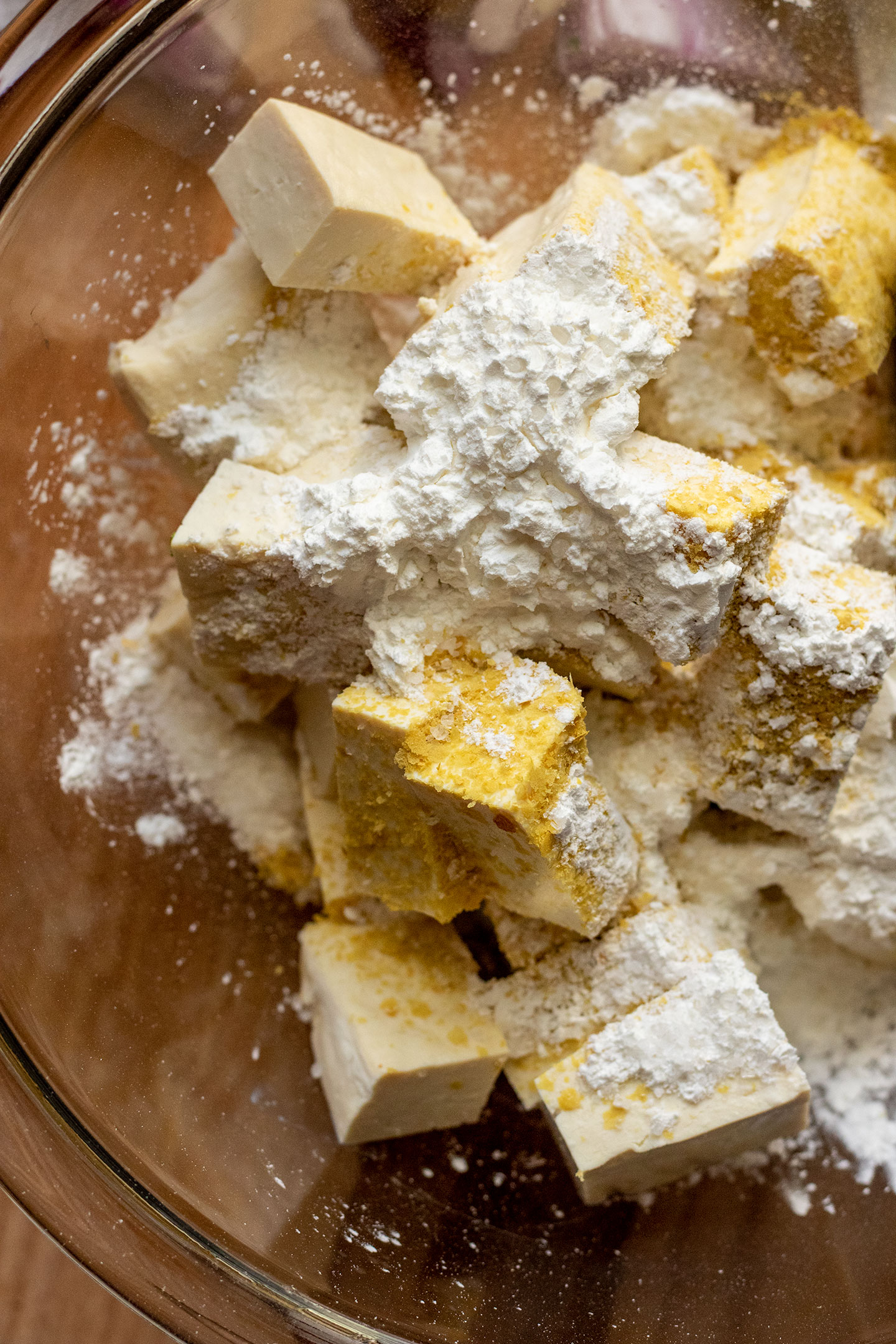 Tofu coated in cornstarch and nutritional yeast being tossed together in a bowl.