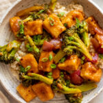 Bowl of orange tofu, broccoli, and onions served over rice in a bowl.