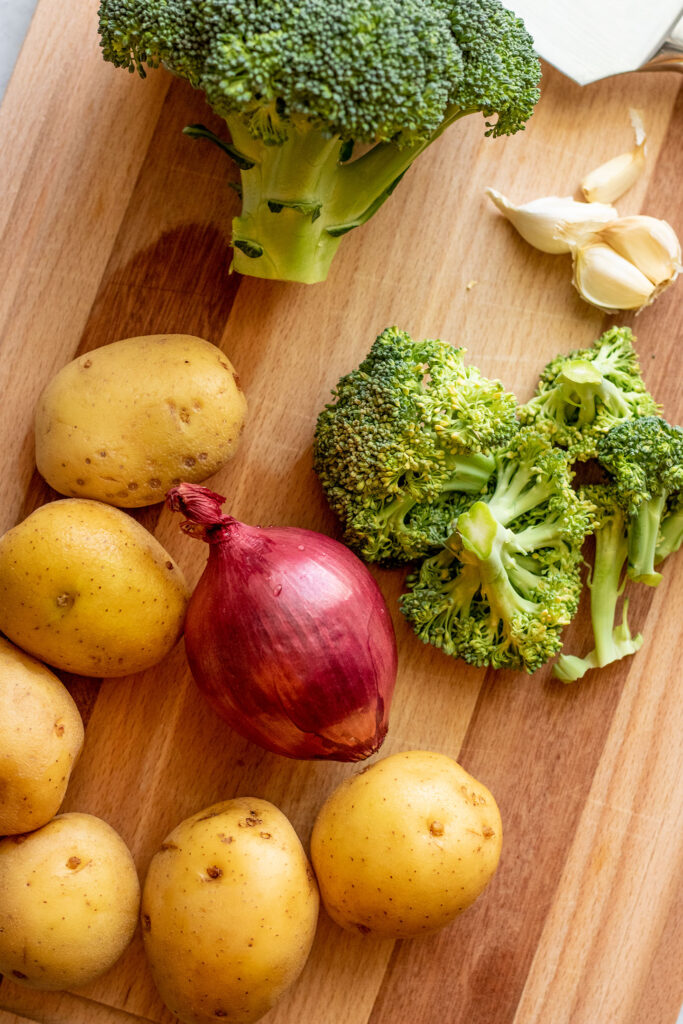 Yukon gold potatoes, onion, broccoli and garlic resting on a cutting board.