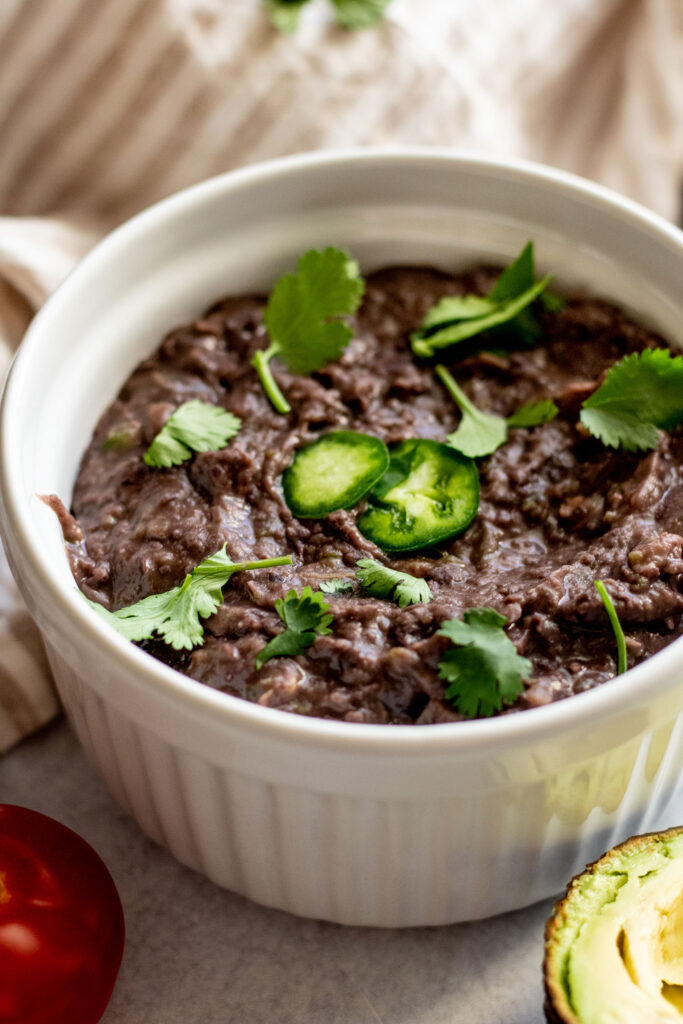 Side view of a bowl of refried black beans topped with jalapeno slices and cilantro.