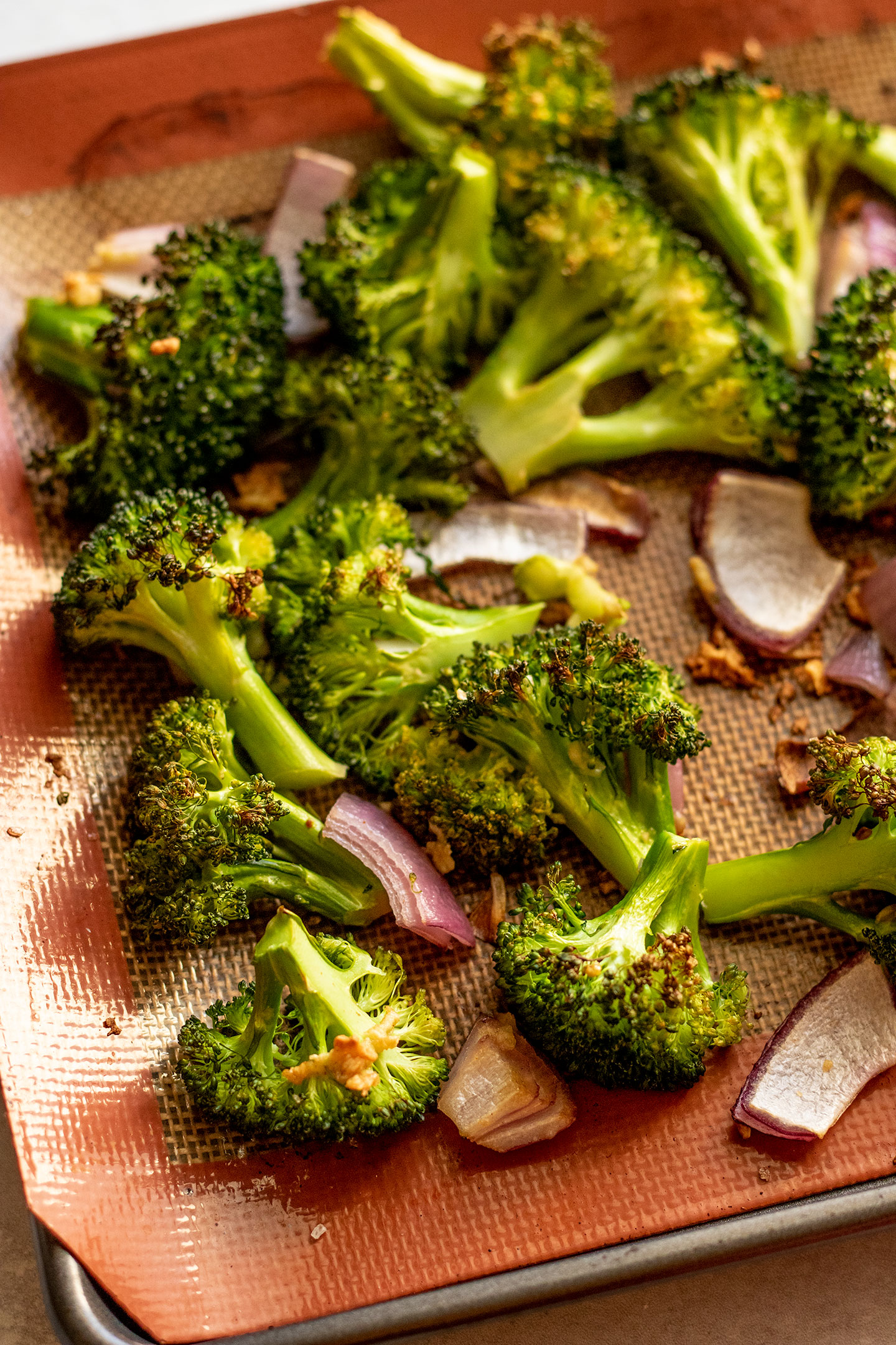 Roasted broccoli, onions and garlic on a baking tray.