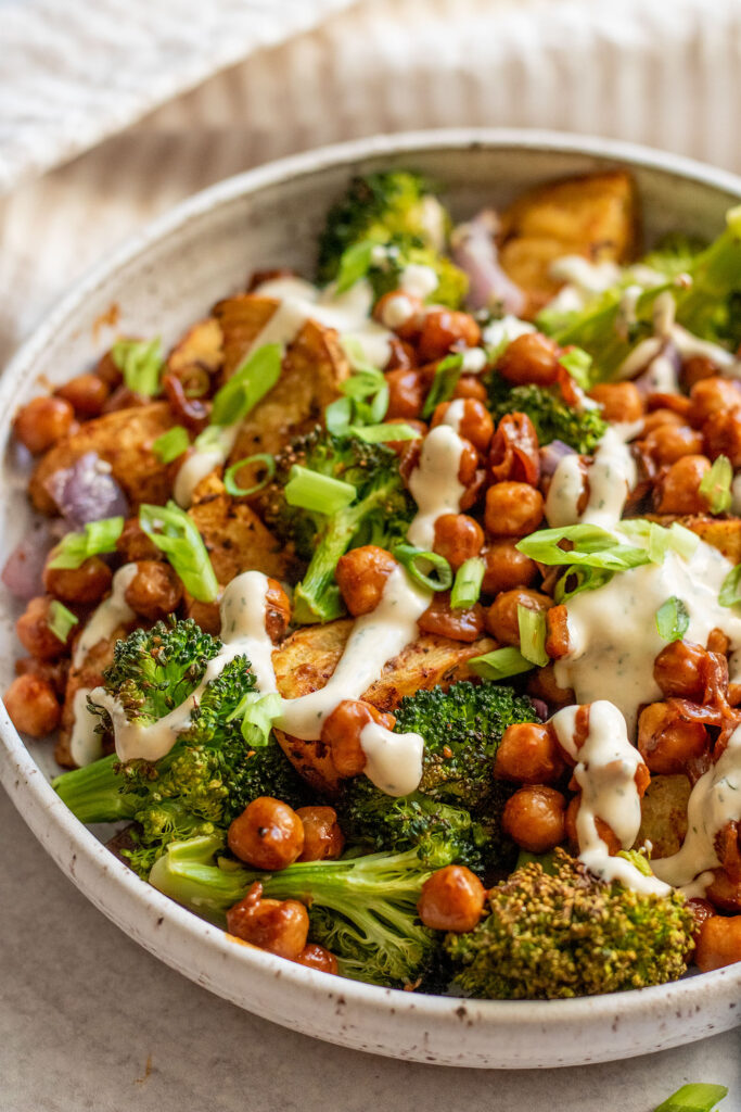 Side view of a bowl of potatoes, broccoli and chickpeas coated with tahini sauce.