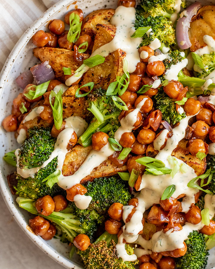 Big bowl filled with roasted potatoes, broccoli, and chickpeas with a drizzle of tahini sauce on top.