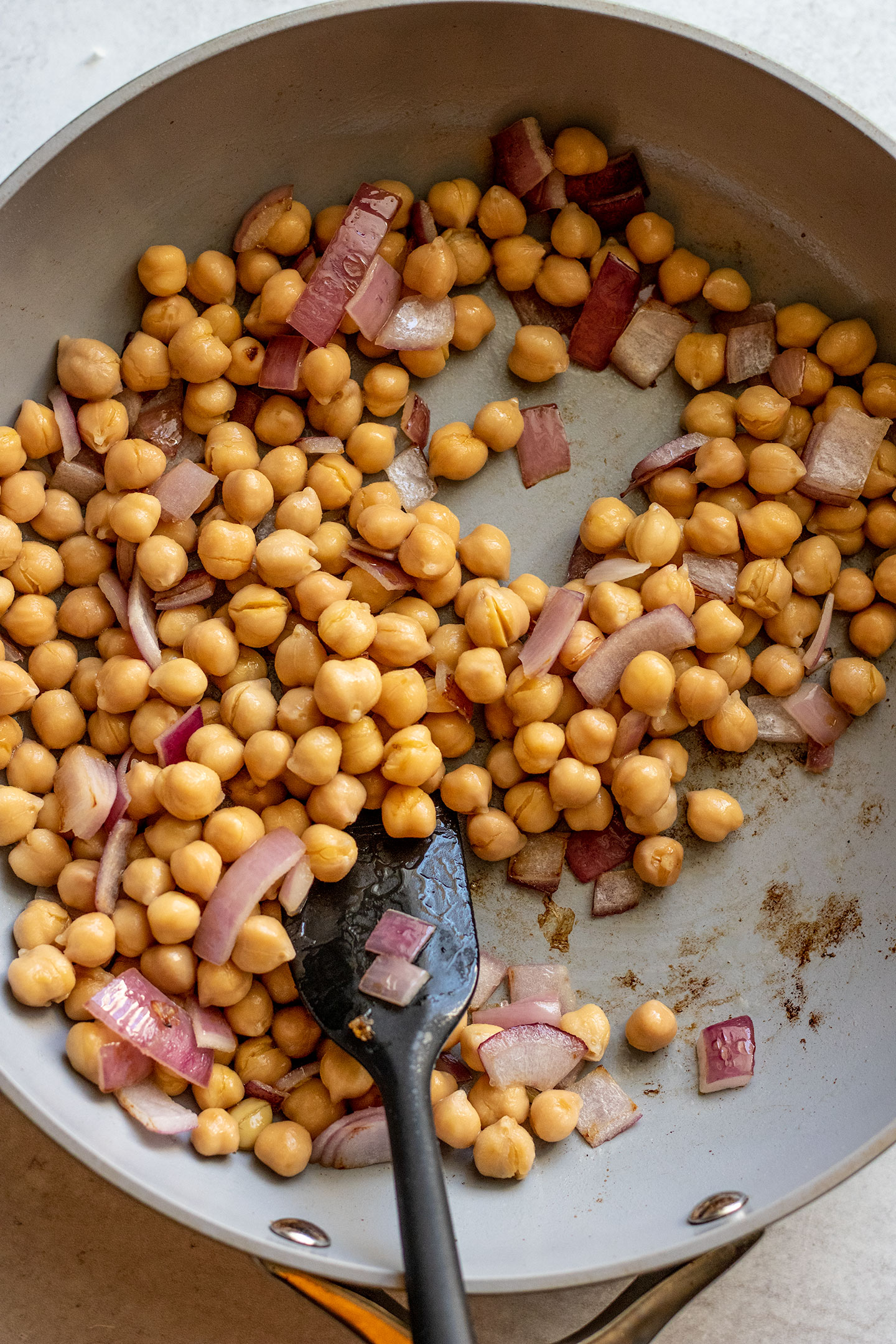 Chickpeas sauteing in a pan with onions and garlic.